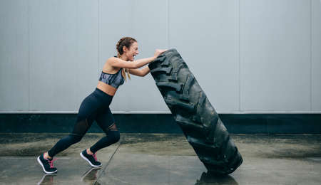 Young sportswoman doing cross-training lifting a tire on a rainy dayの写真素材