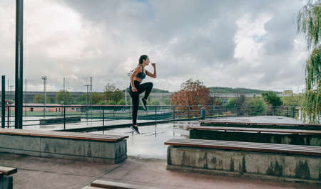 Young girl jumping on benches doing outdoor training on rainy day