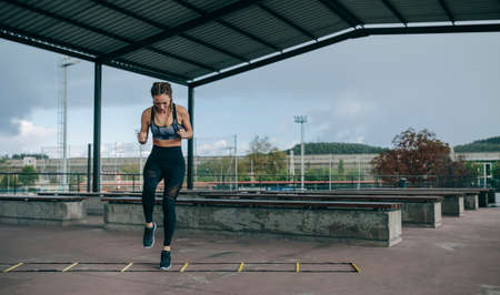 Young sportswoman training jumping on an agility ladder outdoorsの写真素材