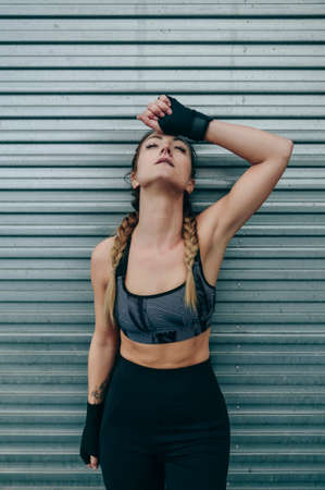 Exhausted sportswoman resting supported on a metal wall outdoors