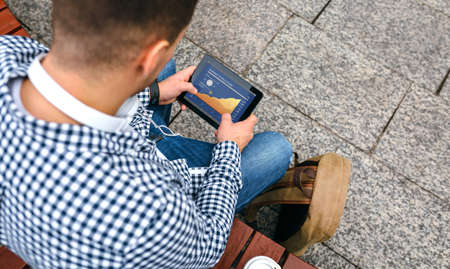 Top view of unrecognizable young man looking cryptocurrencies in tablet outdoorsの写真素材