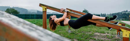 Athlete woman training hanging on a wooden bar in a park
