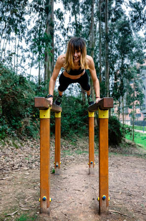 Happy athlete woman training on parallel bars in a park