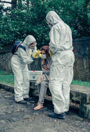 Doctors putting protective mask on woman infected by a virus outdoors