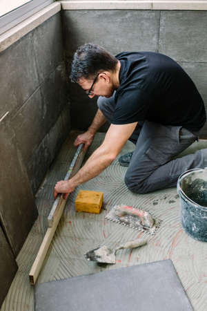 Bricklayer checking the floor with a level to install a tile floorの写真素材