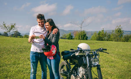 Young couple looking mobile with a motorcycle outdoors