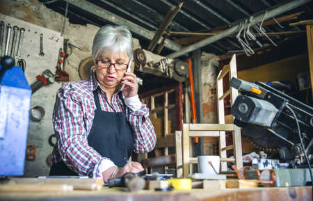 Senior female carpenter talking on the phone in her workshopの写真素材