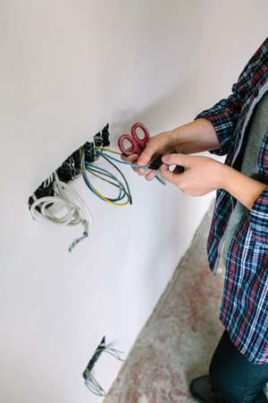 Unrecognizable female electrician wrapping cable with electrical tape on the electrical installation of a houseの写真素材