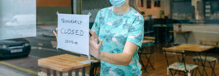 Woman placing a coronavirus closure sign in a coffee shopの写真素材