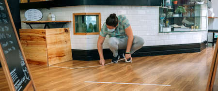 Coffee shop worker putting floor marks to keep social distanceの写真素材