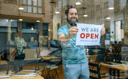 Happy man placing opening poster after coronavirus on the glass of his businessの写真素材