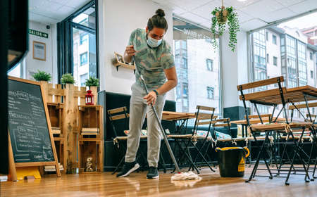 Worker with mask mopping the floor of a restaurant