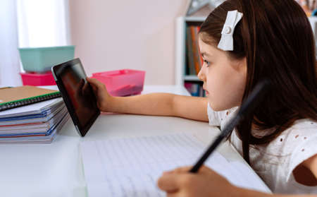 Girl doing homework with the tablet sitting at a desk in her bedroom