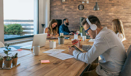 Young man working with tablet and headphones in an office next to his colleaguesの写真素材