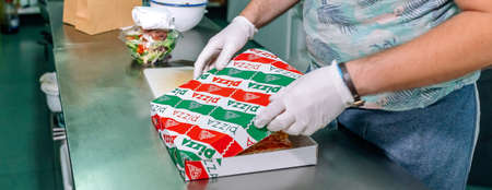 Unrecognizable cook in restaurant kitchen preparing pizza to takeaway