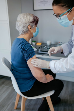 Senior woman being vaccinated against coronavirus by a female doctorの写真素材