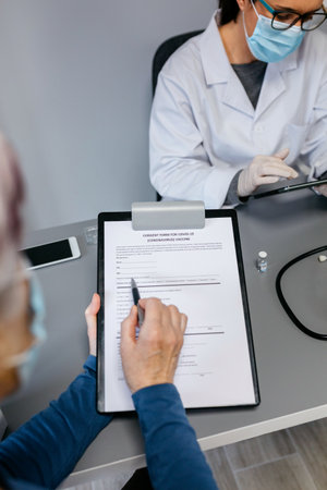 Woman reading consent form for coronavirus vaccine with her doctor