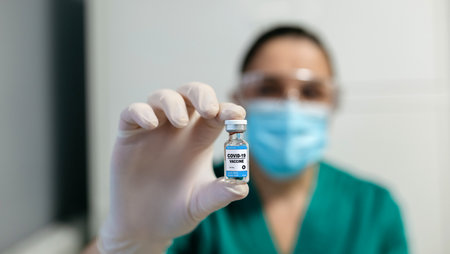 Unrecognizable female laboratory technician showing vial of coronavirus vaccine. Selective focus on...