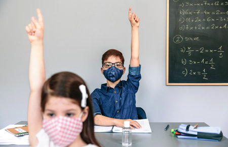 Students with face masks raising their hands at schoolの写真素材