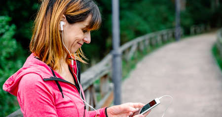 Athlete woman with earphones looking an app on mobile outdoors