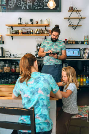 Mother drawing with her daughter while father works in their own coffee shop. Reconciliation family life work conceptの写真素材