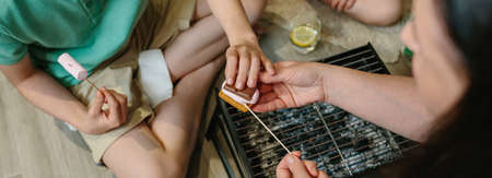 Top view of unrecognizable family making smores with small barbecue at homeの写真素材