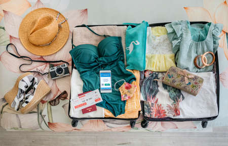 Open suitcase with woman luggage for beach vacation and digital health passport on mobile phoneの写真素材