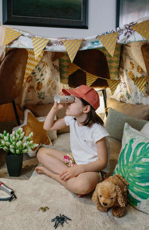 Little girl playing with cardboard binoculars while camping at home in the living roomの写真素材