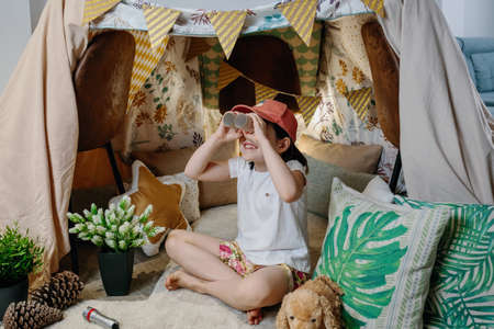 Little girl playing with cardboard binoculars while camping at home in the living roomの写真素材
