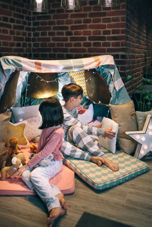 Children preparing tent with chairs and bed sheets for pajama party