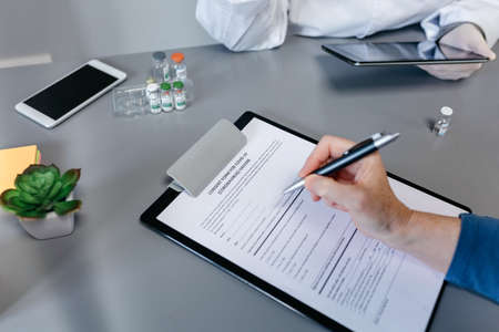 Unrecognizable woman filling in consent form for  vaccine with her doctor