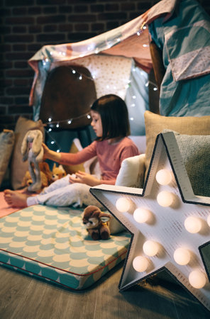 Star lamp craft made with cardboard and pin pong balls with girl playing in a teepee in the background. Selective focus on star lamp in foregroundの写真素材