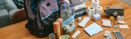 Woman putting cans of food to prepare emergency backpack in living room
