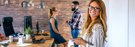 Smiling businesswoman looking at camera in office with colleagues in the background