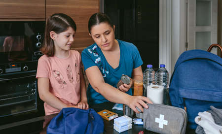 Mother preparing emergency backpack with her daughter in the kitchenの写真素材