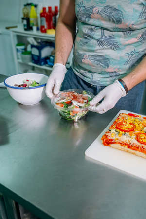 Unrecognizable cook in restaurant kitchen preparing salad to takeawayの写真素材