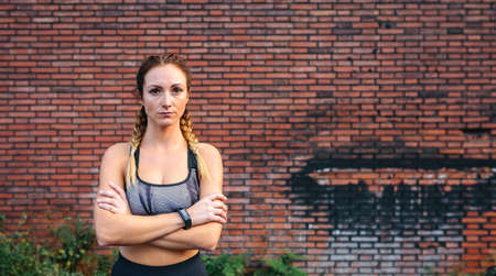 Sportswoman with crossed arms posing in front of a brick wallの写真素材