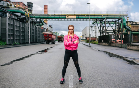 Sporty woman looking camera posing in the middle of the road in front of a factoryの写真素材