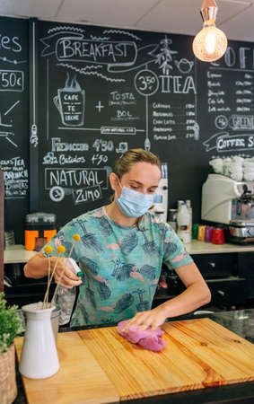 Waitress with mask disinfecting the bar counter due to coronavirusの写真素材