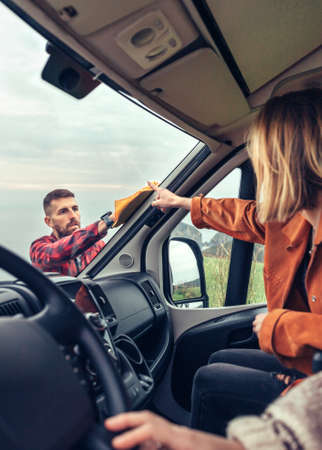 Perfectionist man cleaning motorhome windshield with cloth while woman pointing stainの写真素材