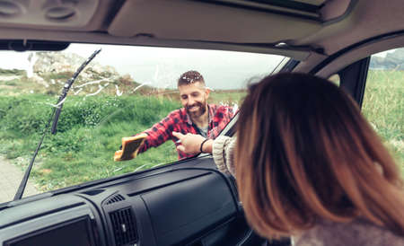 Man smiling cleaning van windshield with cloth while woman pointing stainの写真素材