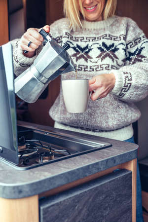 Unrecognizable woman serving coffee with italian coffee maker in camper van in the morning
