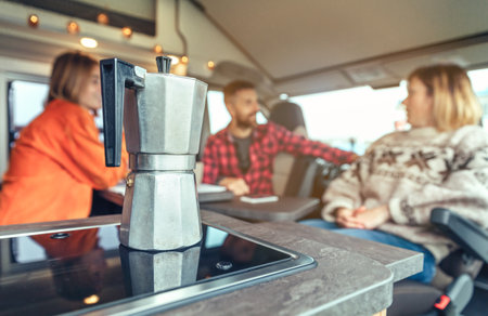 Italian coffee maker with group of people talking in the background in a camper van. Selective focus on coffee maker in the foregroundの写真素材