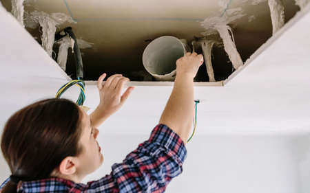 Woman placing tube for kitchen hood installation on kitchen ceilingの写真素材