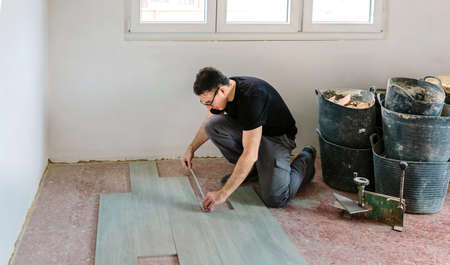 Bricklayer laying and measuring tiles to install a floorの写真素材