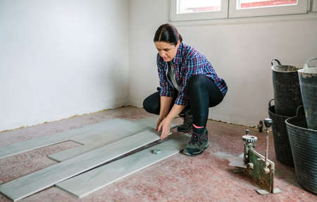 Crouched female bricklayer placing tiles to install a floorの写真素材