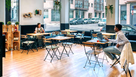 Man and woman talking while working in a coffee shop maintaining social distancingの写真素材