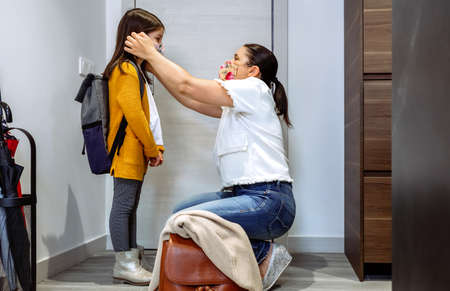 Mother putting the mask on her daughter to go to schoolの写真素材