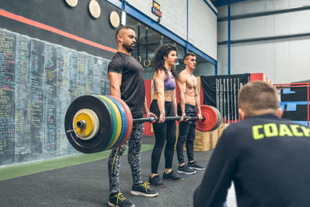 Mixed team lifting weights in the gym while their coach watches themの写真素材