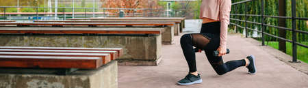 Young woman training doing lunge with dumbbells outdoors